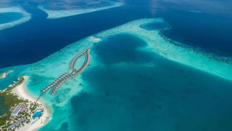 An aerial view of a coastal resort with a long pier, clear turquoise waters, and a sandy beach.