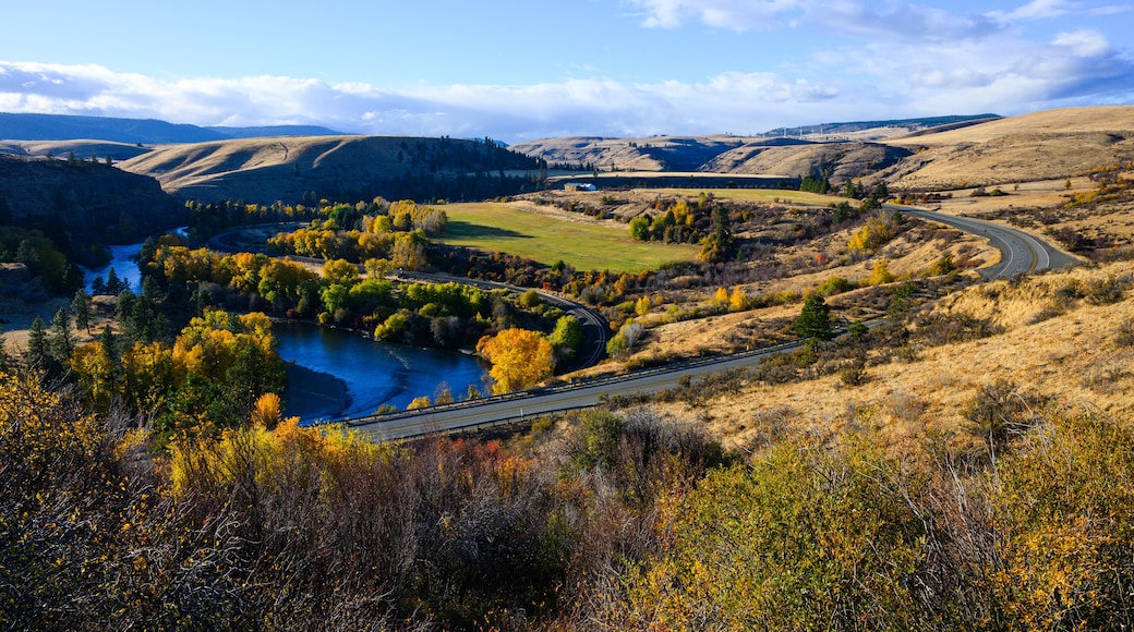 A winding road through a valley with a river, surrounded by hills and autumn-colored trees.