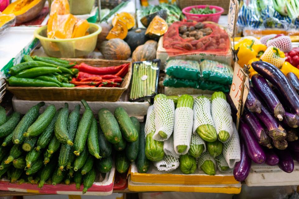 Een verscheidenheid aan verse groenten, zoals komkommers, aubergines en paprika, op een marktkraam.