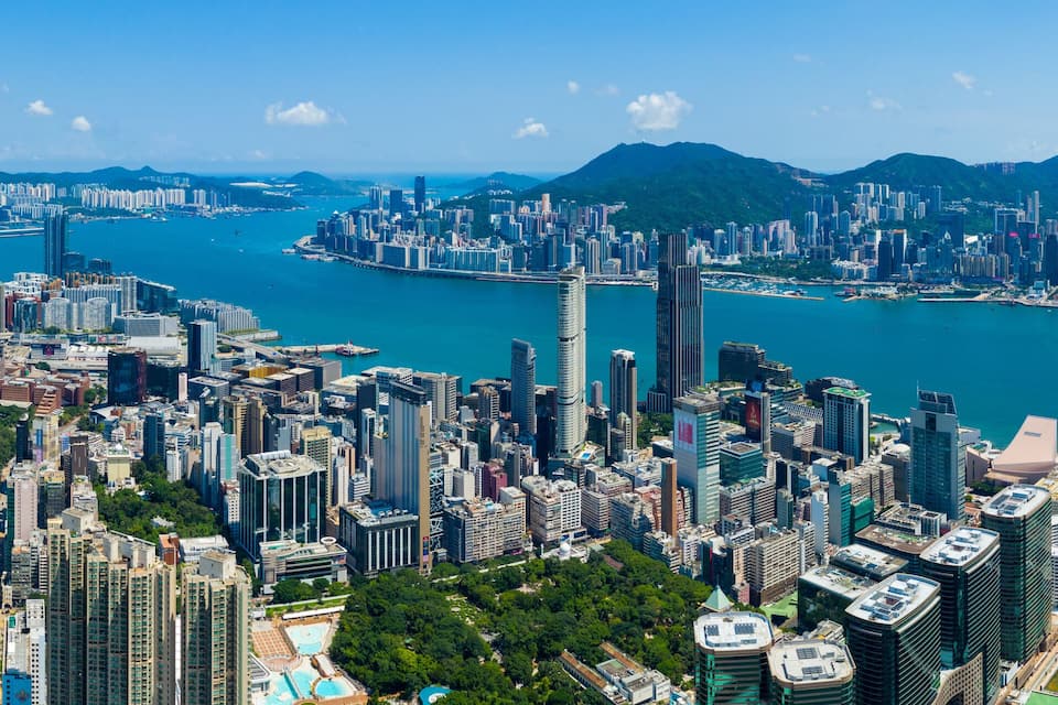 A coastal cityscape with dense high-rise buildings, a large body of water, and distant mountains.