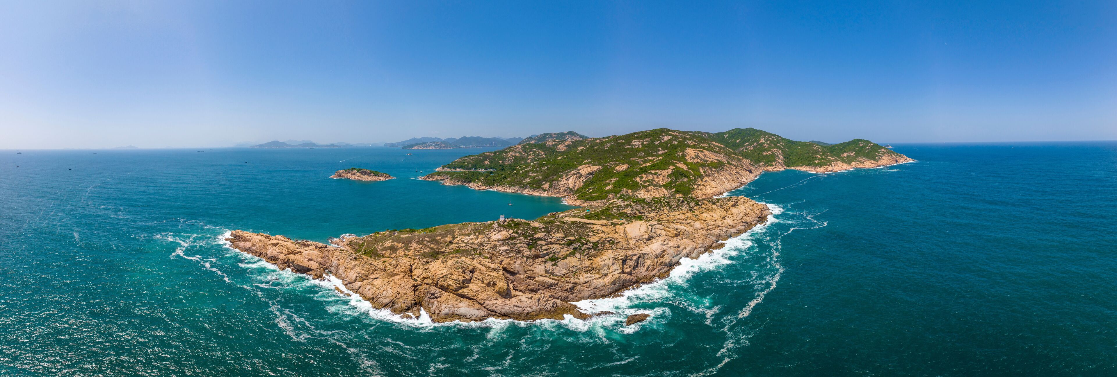 An aerial view of a rugged coastline with rocky terrain and clear blue waters.