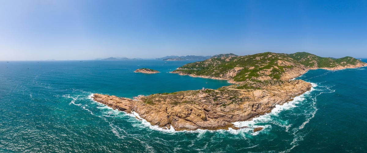 An aerial view of a rugged coastline with rocky terrain and clear blue waters.