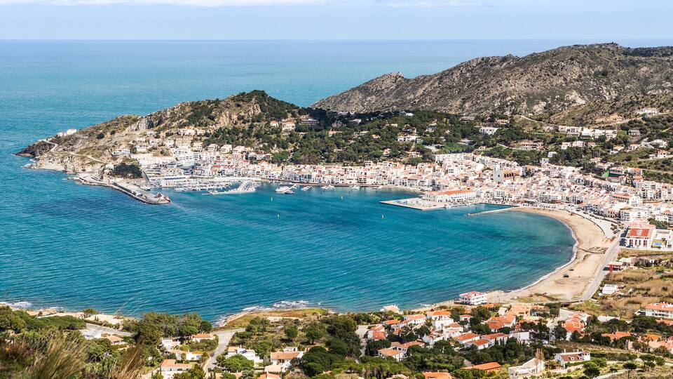 A coastal town with a bay, buildings, and a mountainous backdrop.