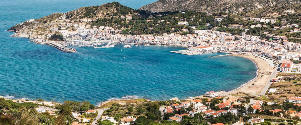 A coastal town with a bay, buildings, and a mountainous backdrop.