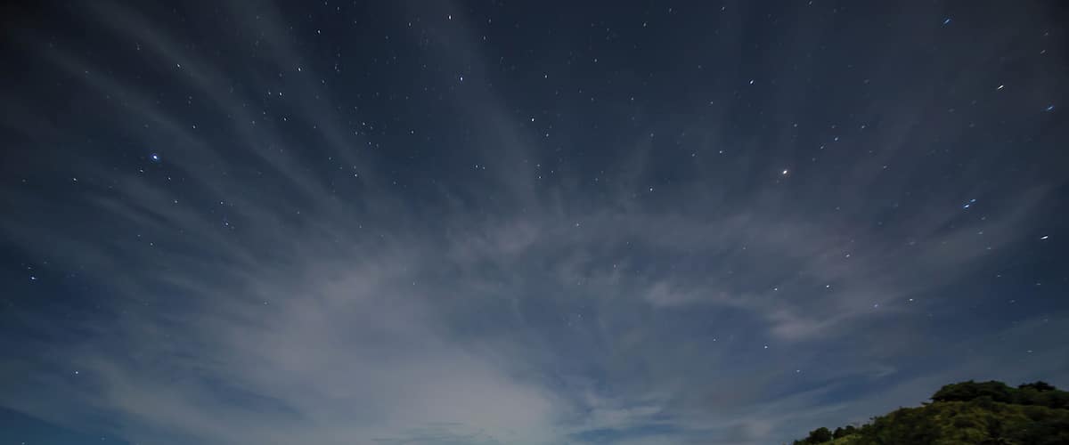 A beach at night with a starry sky and calm water.