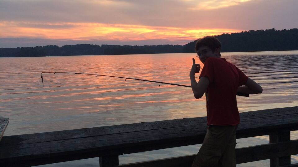 A person fishing on a wooden dock at sunset.