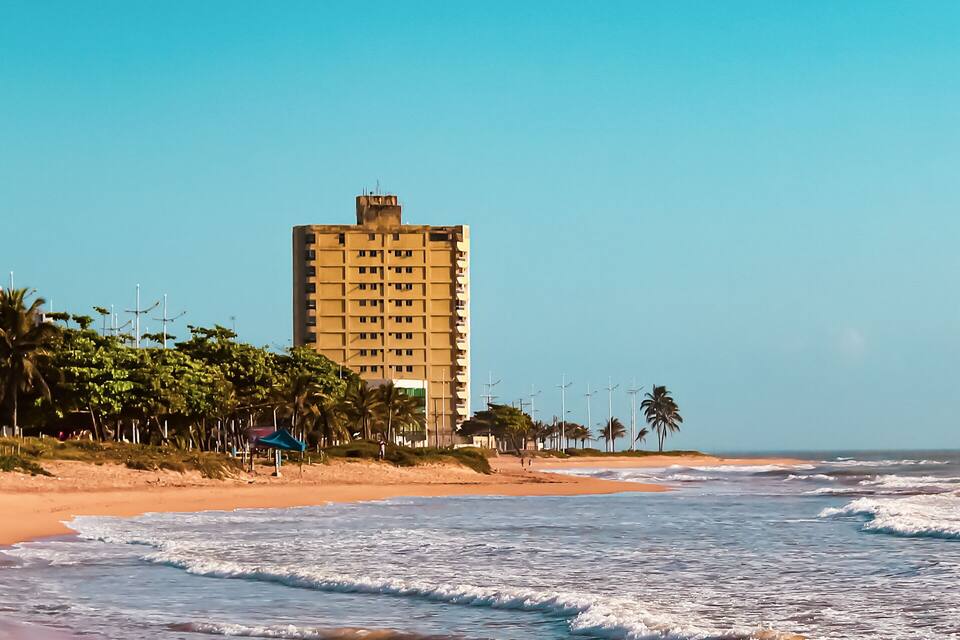 A beach with waves, palm trees, and buildings.