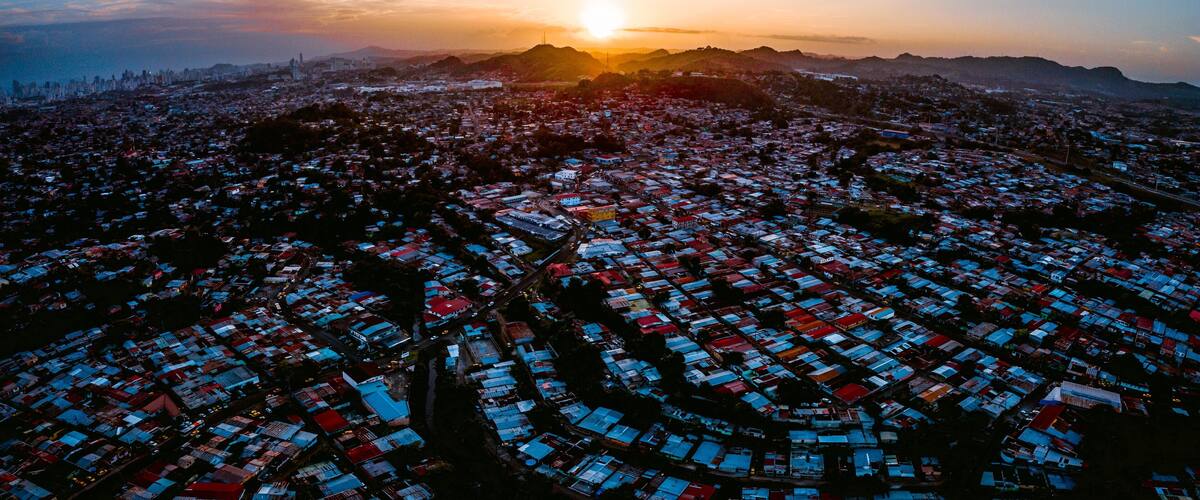 A cityscape at sunset with the sun setting behind a range of hills.