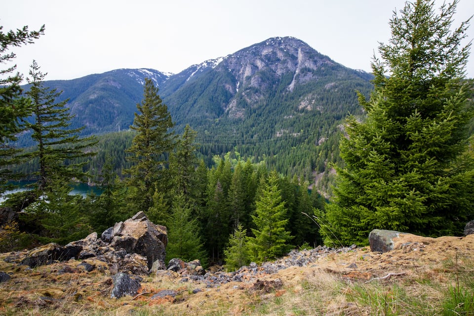 A mountainous landscape with dense forests, rocky terrain, and a lake in the valley.