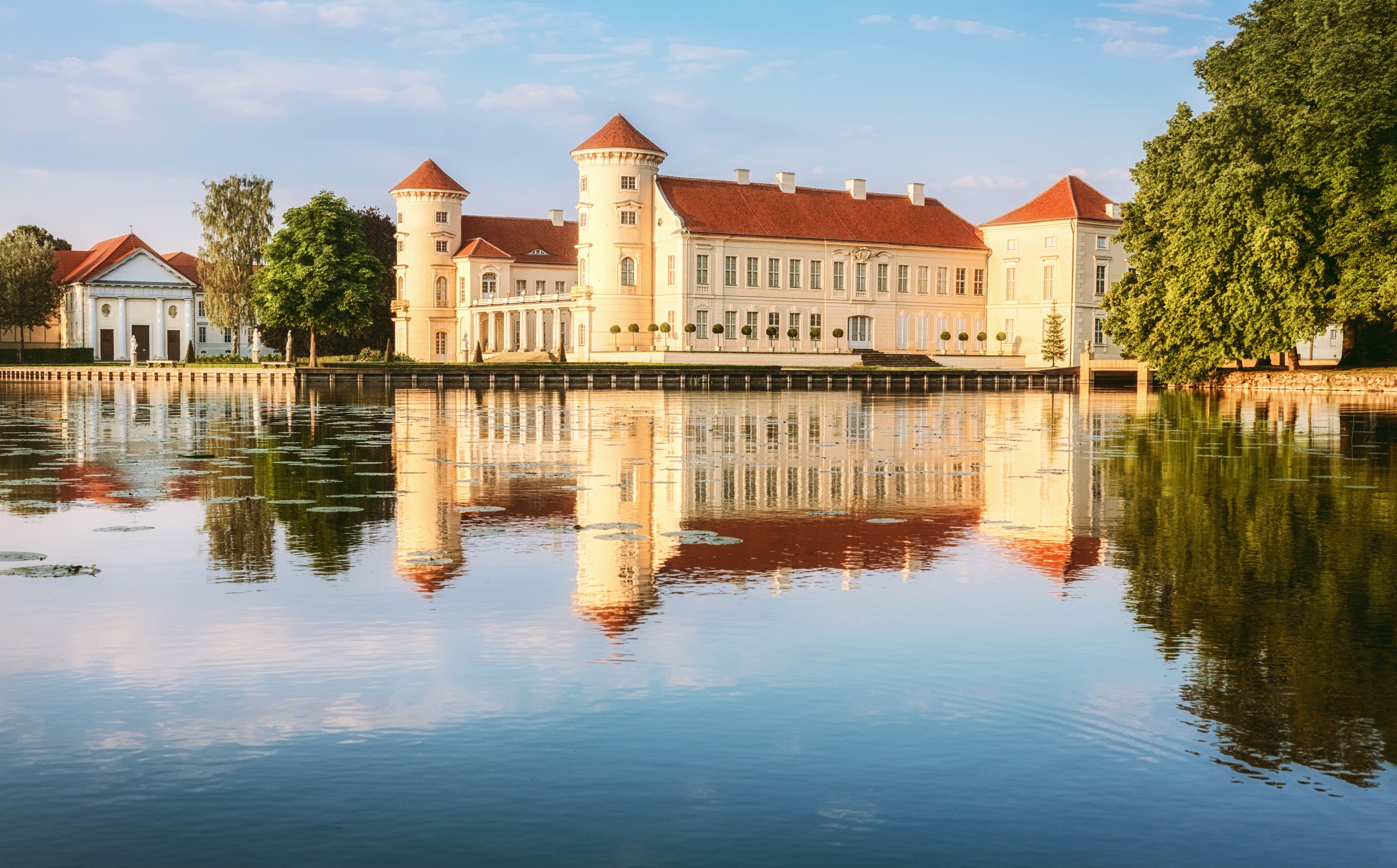 A historic castle with a moat, red-tiled roofs, and a reflection in the water.