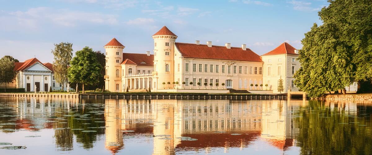 A historic castle with a moat, red-tiled roofs, and a reflection in the water.