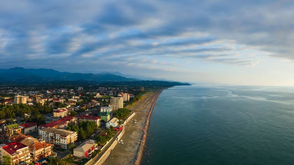 A coastal cityscape with a beach, buildings, and mountains in the background.