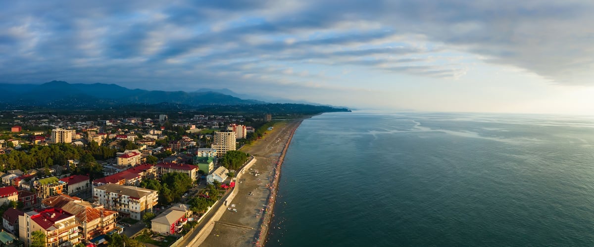 A coastal cityscape with a beach, buildings, and mountains in the background.
