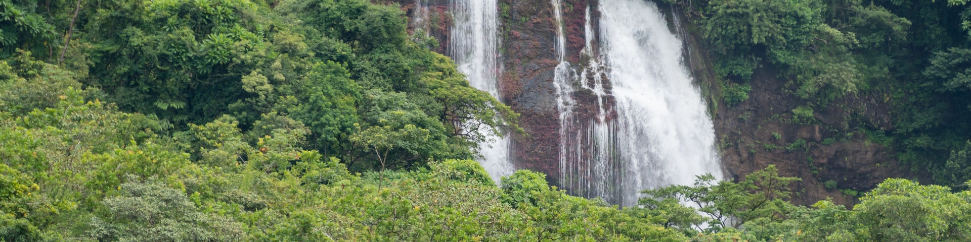 A waterfall cascading down a rocky cliff surrounded by dense green foliage.