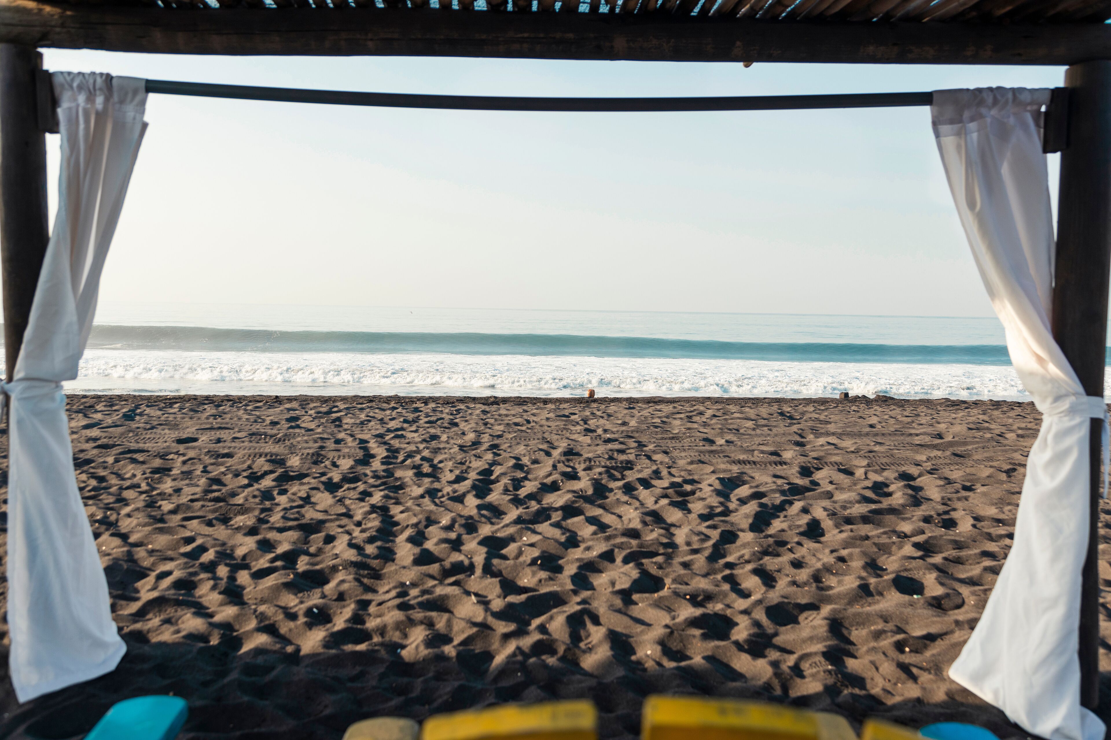 A beach with a wooden structure and white curtains.