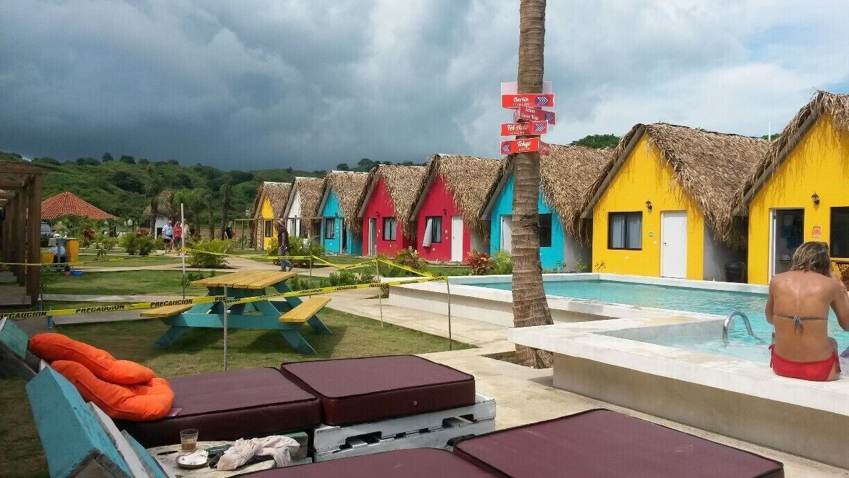 Colorful thatched-roof huts, a swimming pool, and a tropical landscape.