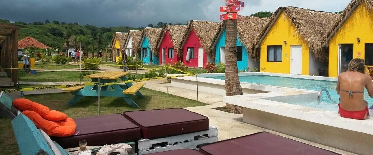 Colorful thatched-roof huts, a swimming pool, and a tropical landscape.