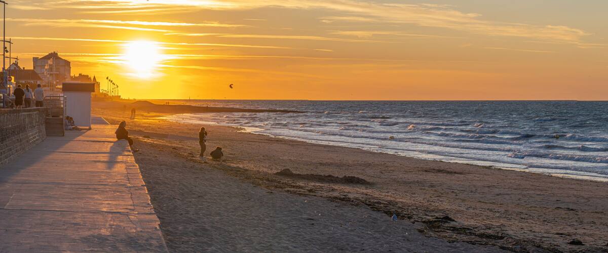 A beach at sunset with waves, a pier, and a lighthouse.