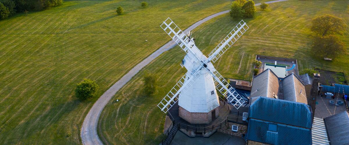 A windmill in a rural landscape with fields and a small building nearby.
