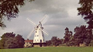 A windmill in a grassy field with trees in the background.