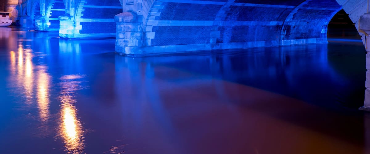 A stone bridge with arches over a body of water, illuminated by street lamps.
