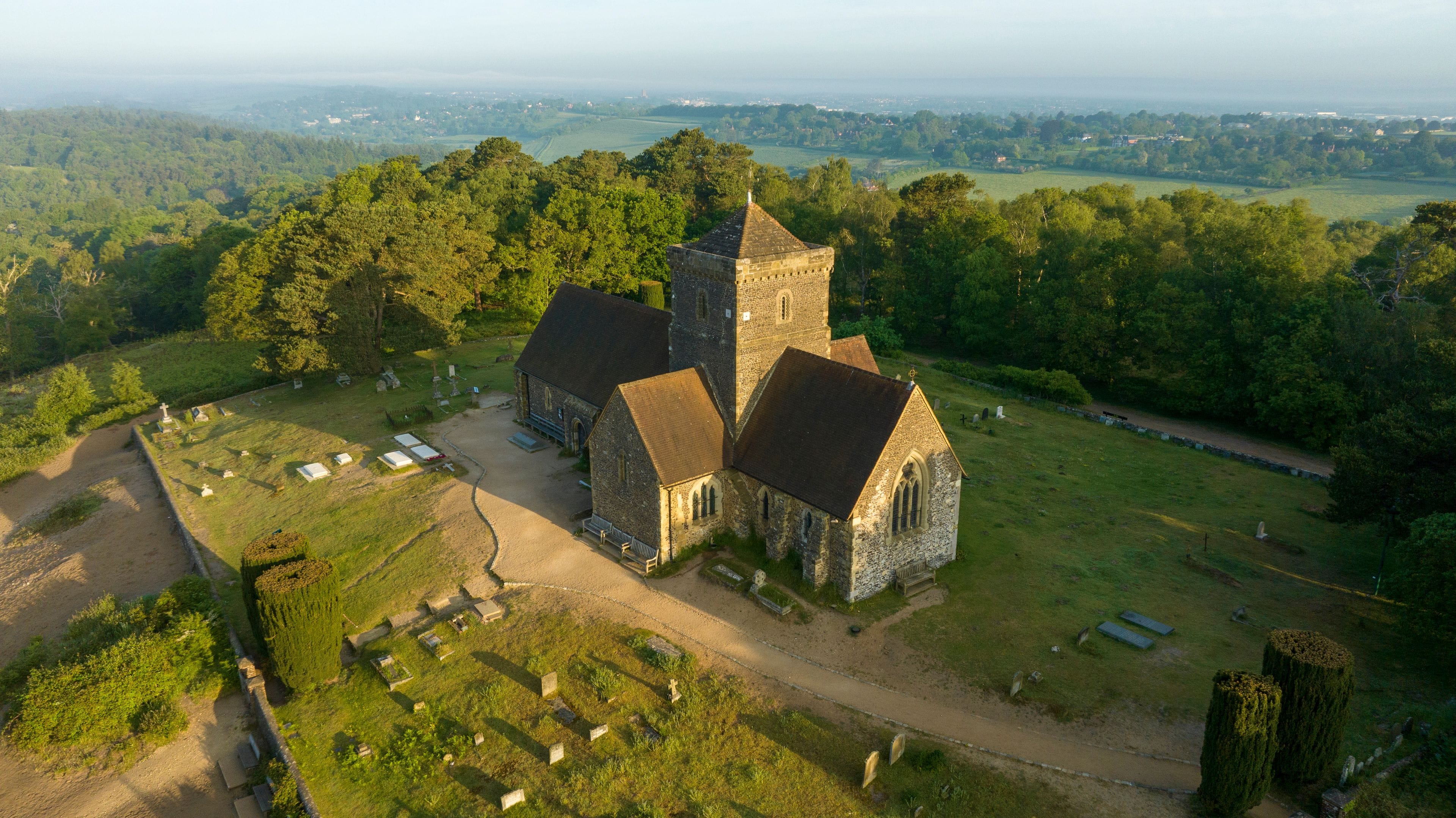 Une église dotée d’un clocher imposant, entourée d’un cimetière et d’une végétation luxuriante.