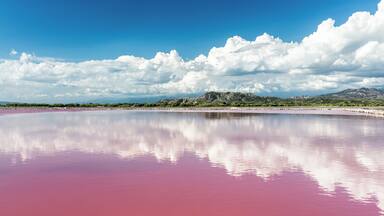 A pink lake with mountains in the background and a clear blue sky.