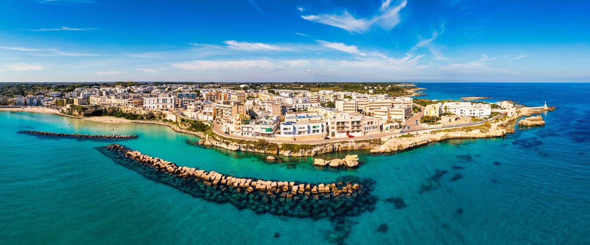 A coastal town with a rocky breakwater, clear turquoise waters, and a mix of residential buildings.