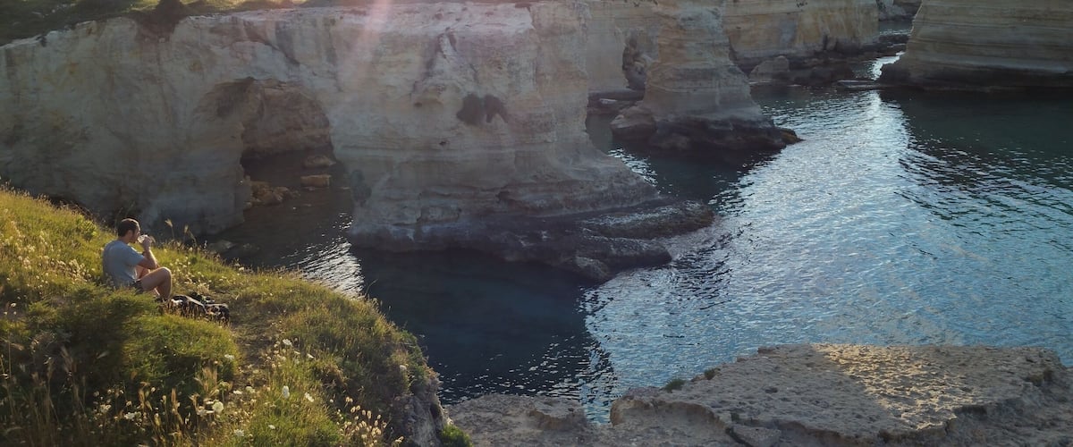 A coastal cliff with a person sitting on the edge.