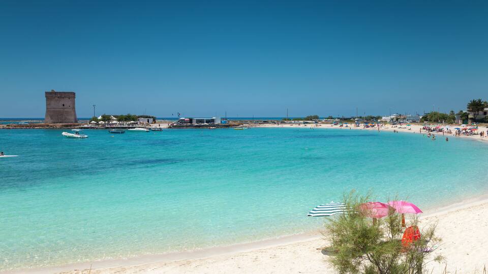 A beach with clear turquoise water, a sandy shore, and a tower in the background.