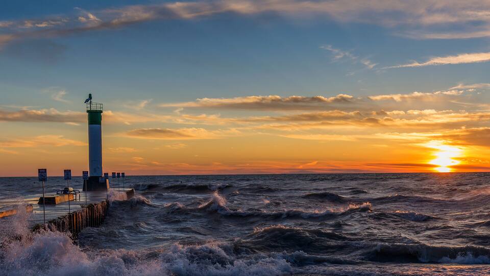 A lighthouse at sunset with rough sea waves.