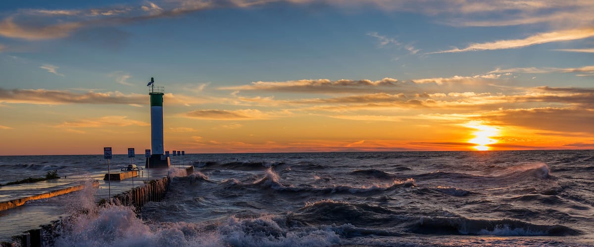 A lighthouse at sunset with rough sea waves.