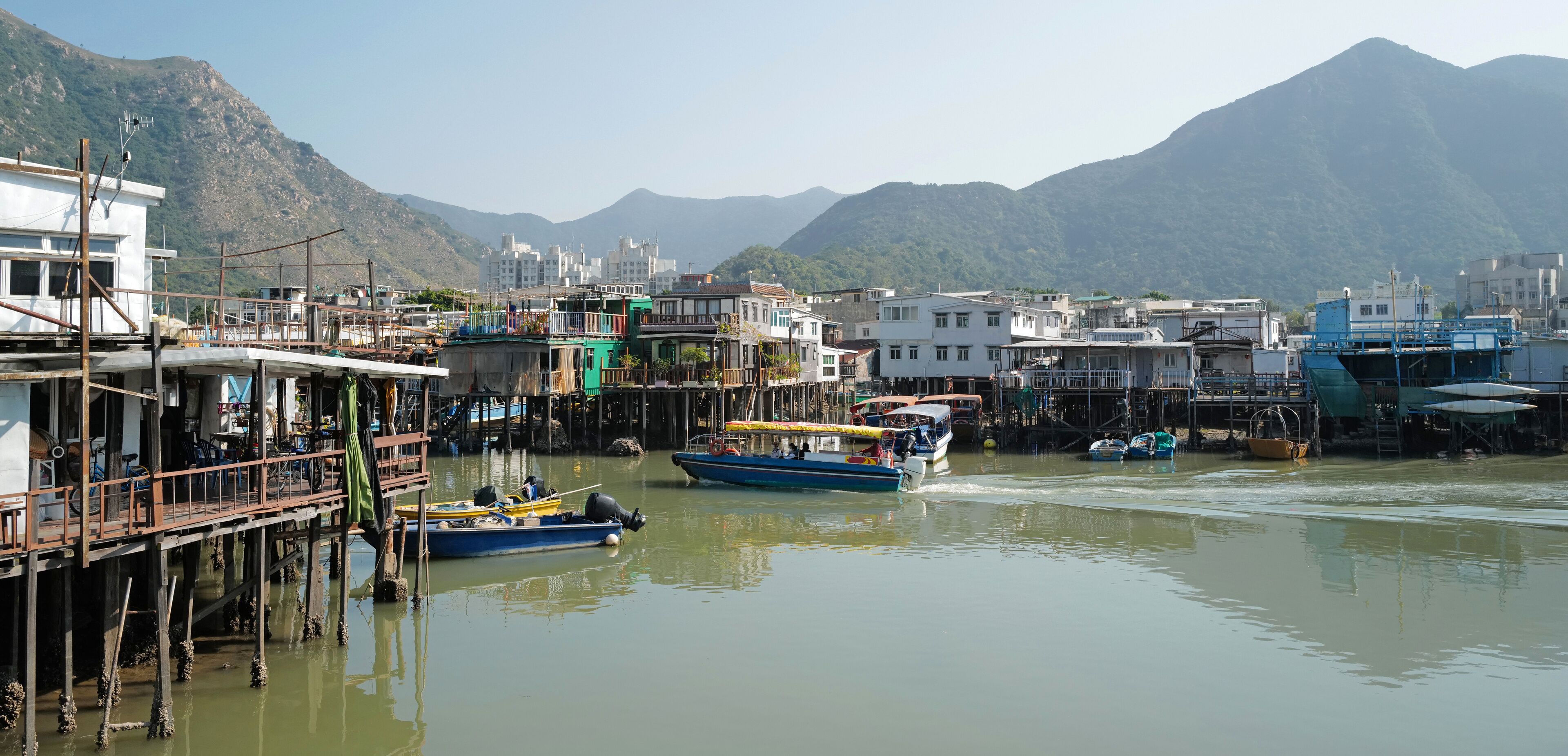 A waterfront with boats, buildings, and mountains in the background.