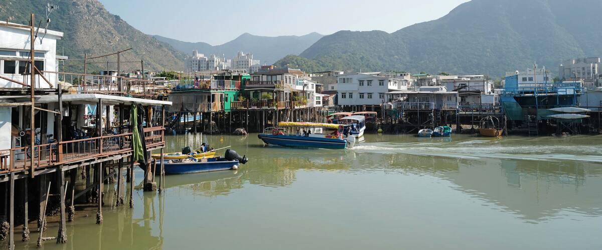 A waterfront with boats, buildings, and mountains in the background.