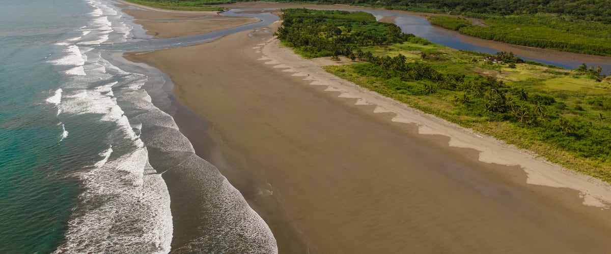 A coastal landscape with a sandy beach, a river, and green vegetation.
