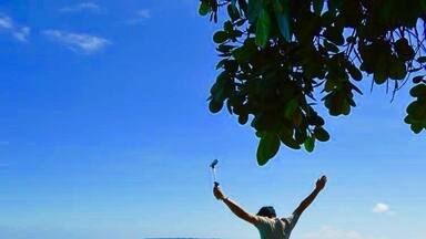 A person standing on a concrete edge with arms raised, overlooking a clear blue ocean.