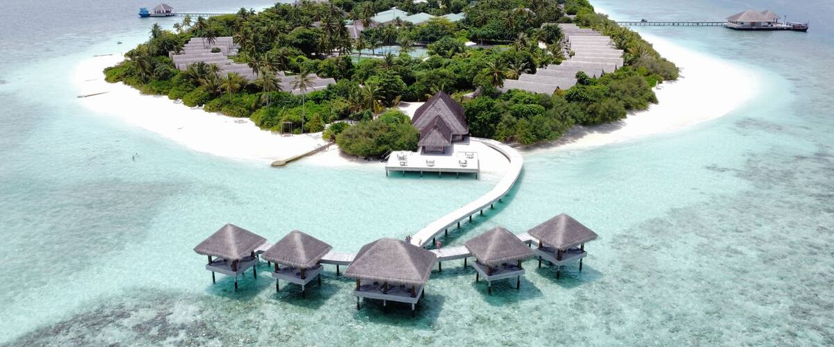 An overwater bungalows on a small island surrounded by turquoise waters.