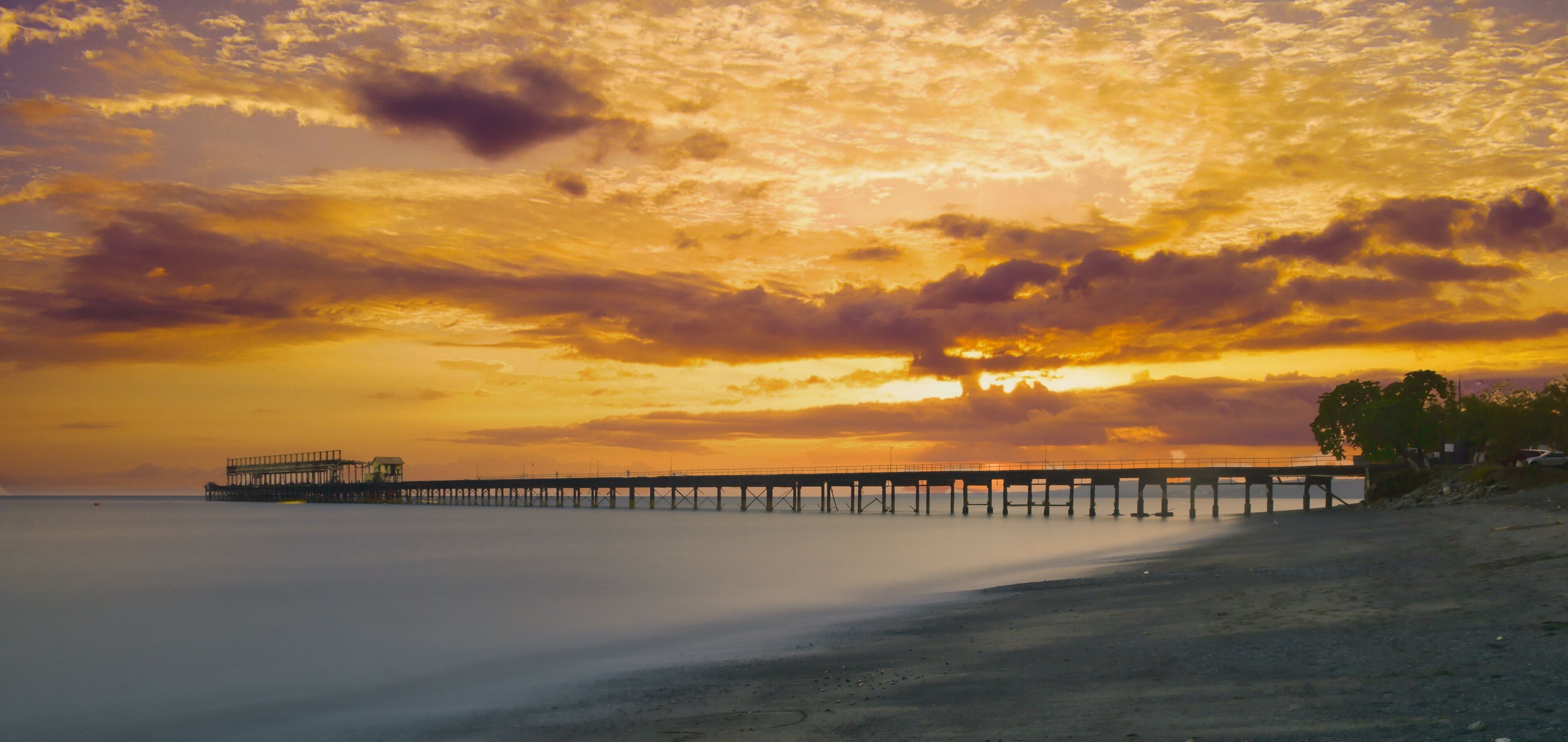 A sunset over a beach with a pier extending into the water.