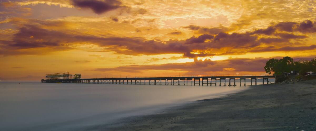 A sunset over a beach with a pier extending into the water.