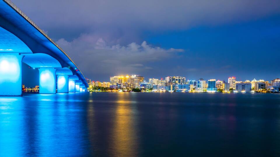A nighttime cityscape with a prominent illuminated bridge and a skyline of buildings.