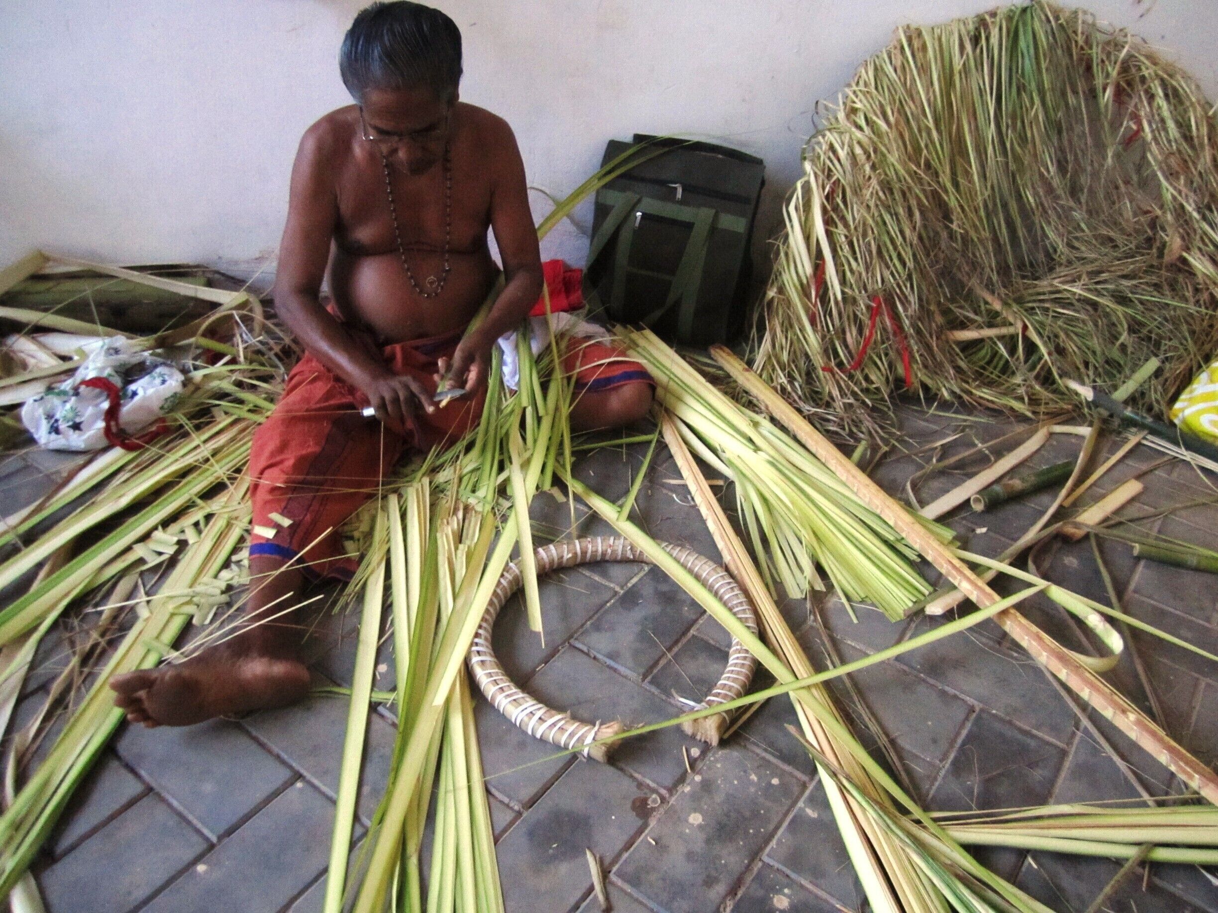 A person sitting on the floor surrounded by cut stalks of grass.