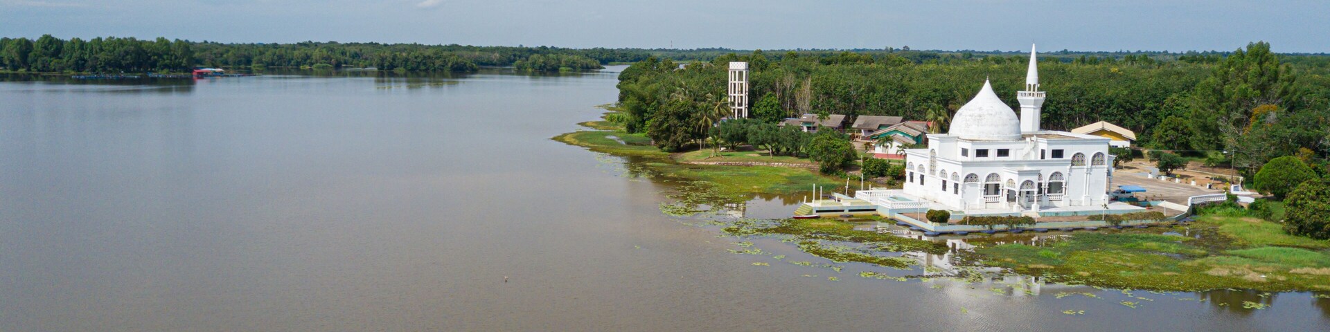 Una mezquita blanca con un minarete sobre una pequeña isla en un río tranquilo.