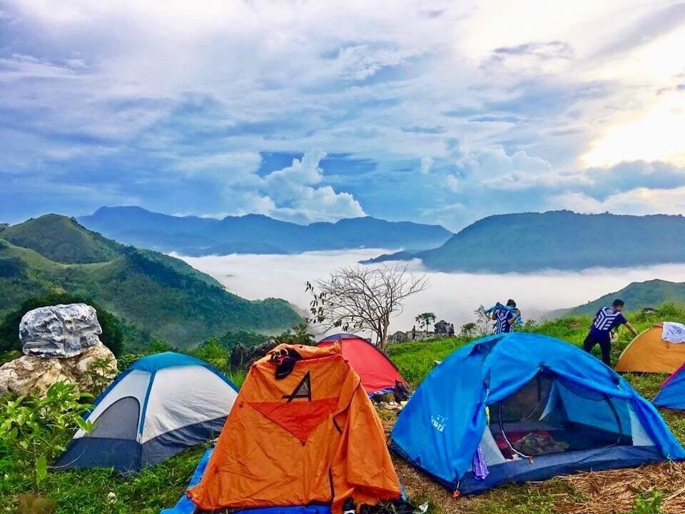 A group of tents on a grassy hill with a lake and mountains in the background.