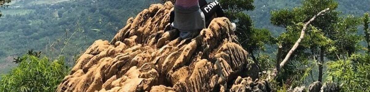 A person standing on a rocky outcrop with arms raised, overlooking a valley with a winding river and distant mountains.