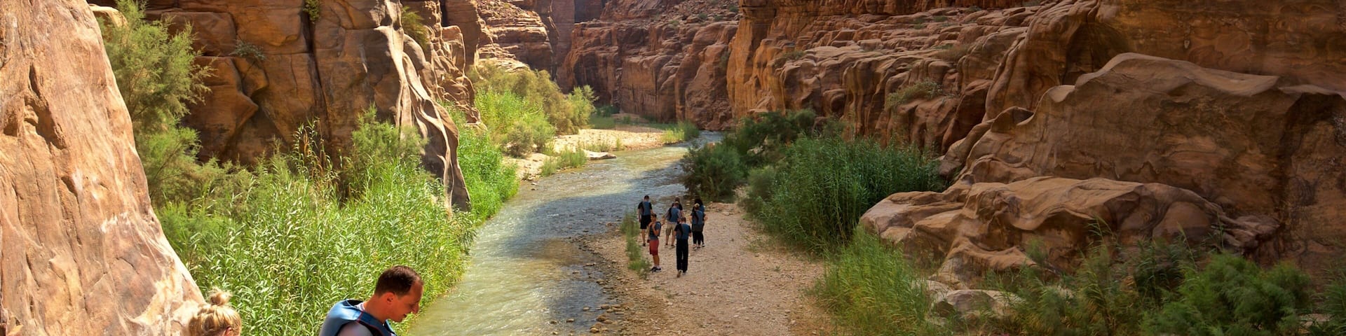 A canyon with a river, rocky cliffs, and people hiking.