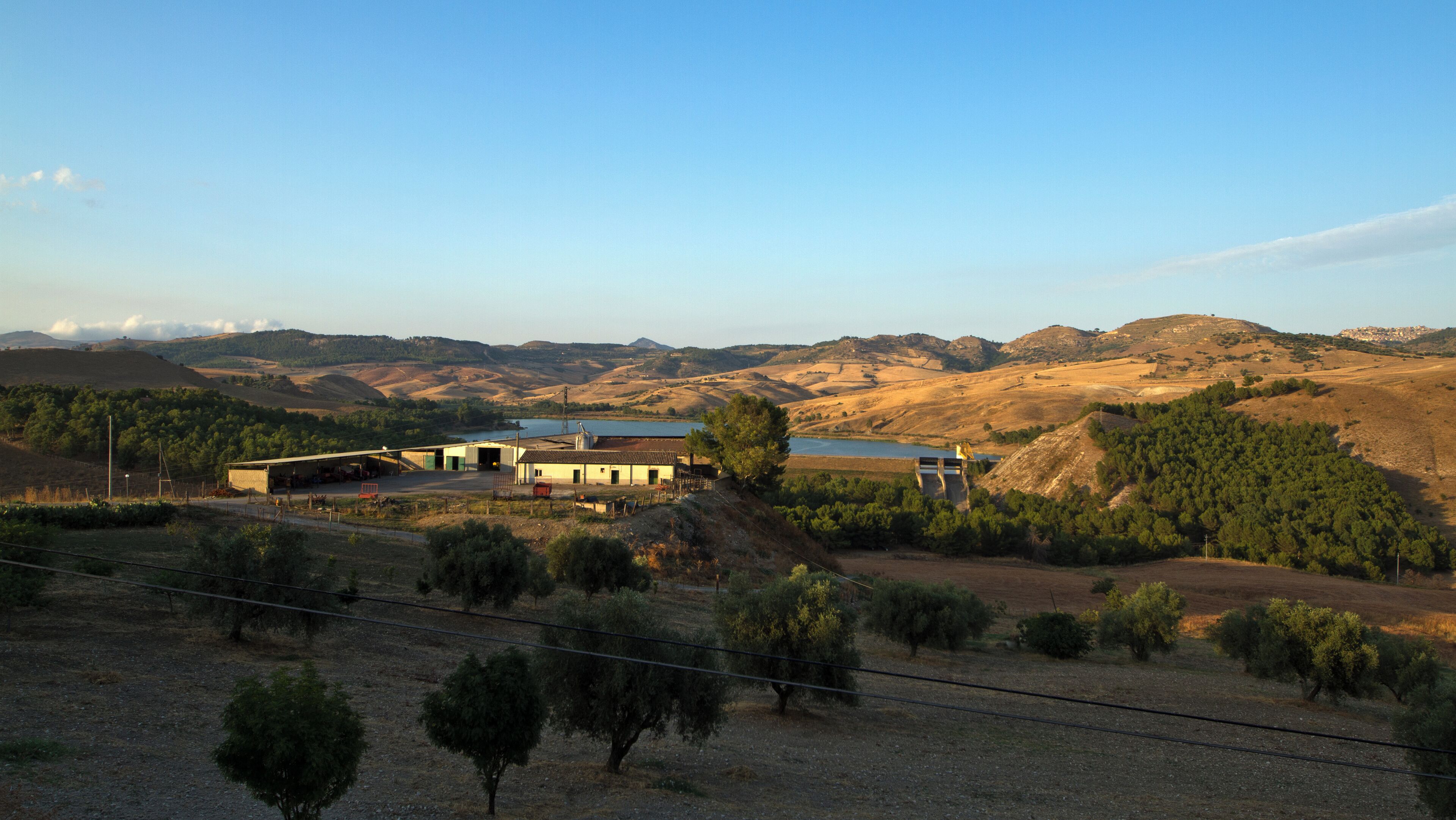 A rural landscape with a house, a body of water, and rolling hills.