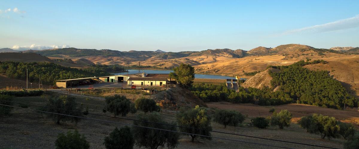 A rural landscape with a house, a body of water, and rolling hills.