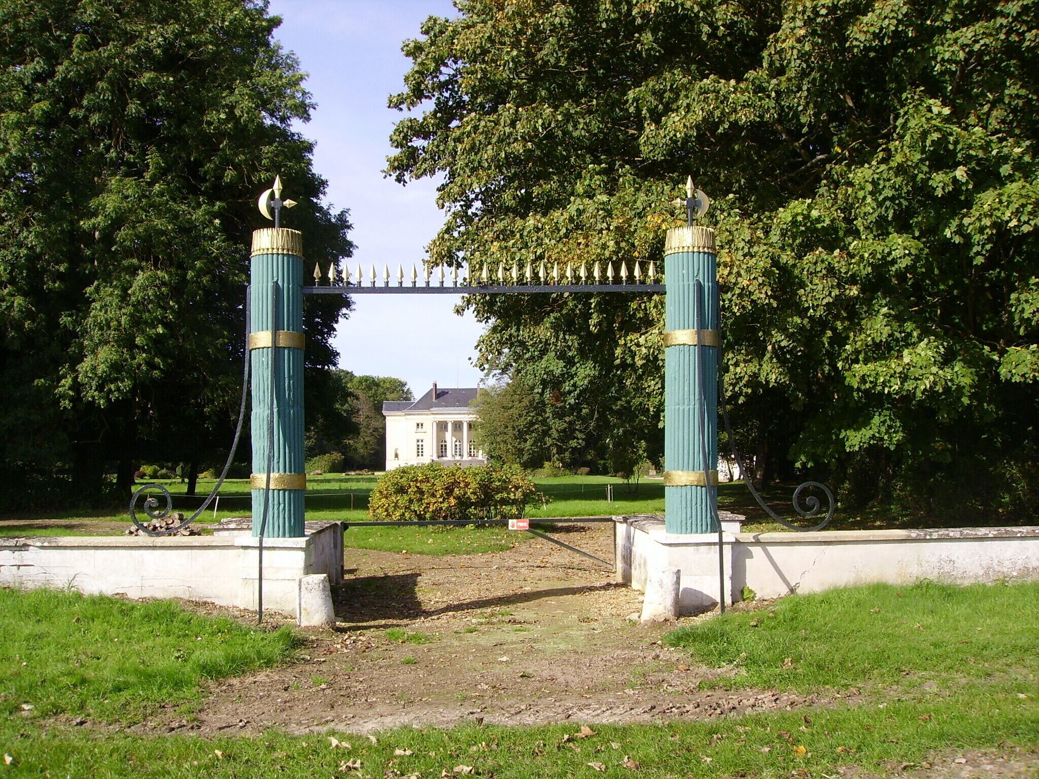 A park entrance with a decorative gate, a building in the background, and lush greenery.
