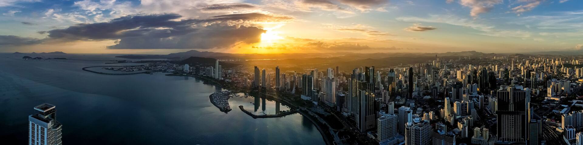 A coastal cityscape with a sunset, high-rise buildings, and a marina.