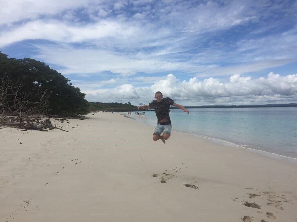 A person jumping on a sandy beach with a calm sea and a cloudy sky in the background.